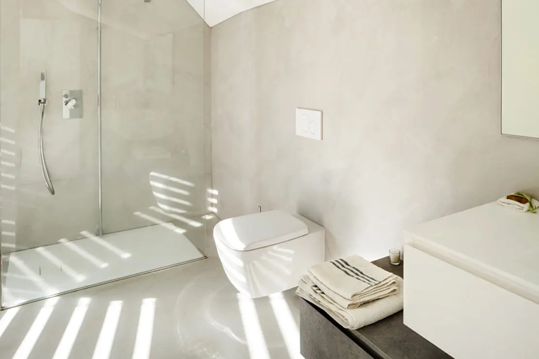 Baño con piso y muros de microcemento en tonalidad suave.